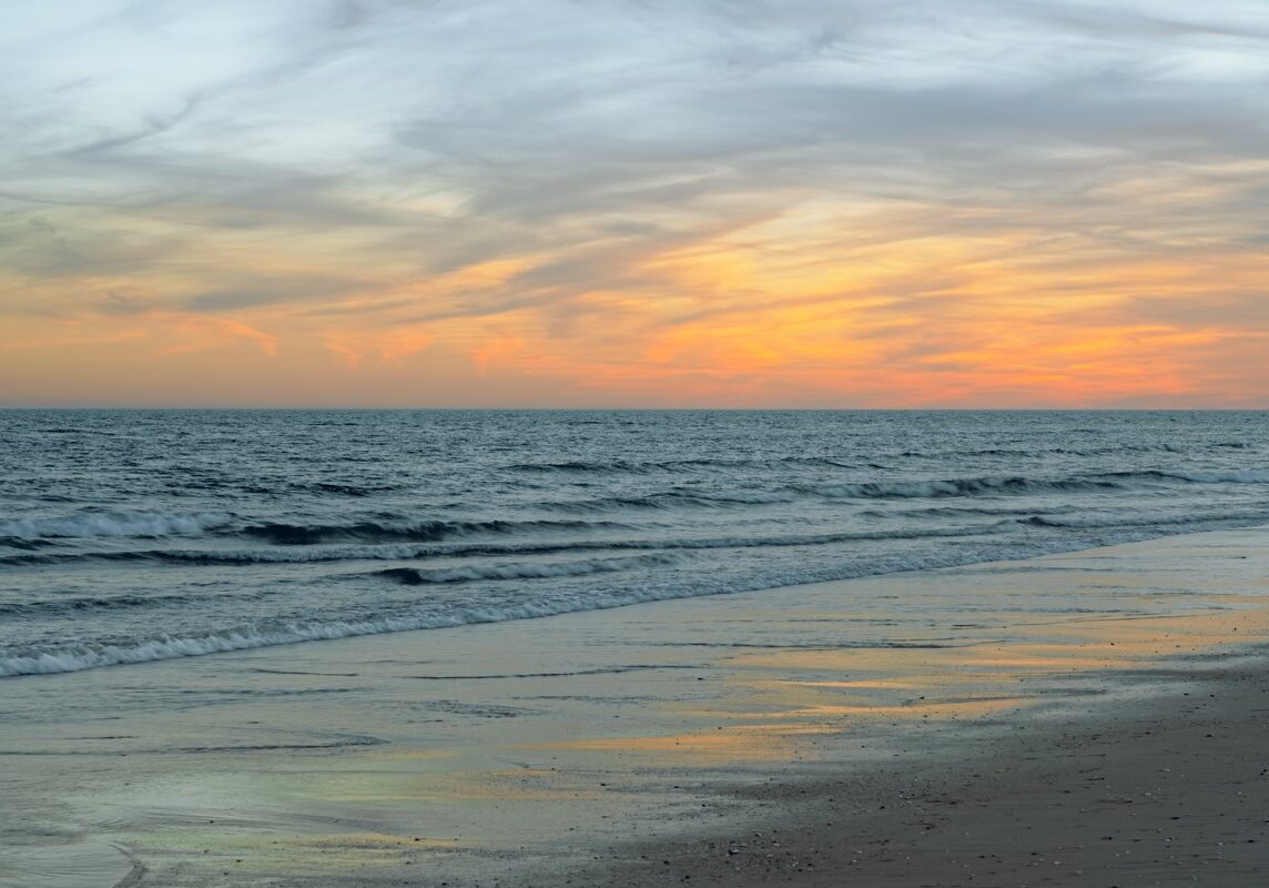 Calm waves roll onto the beach as pastel colors fill the sky at twilight.