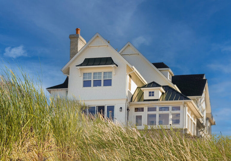 a white shingled beach home with beach grass in foreground against a blue sky